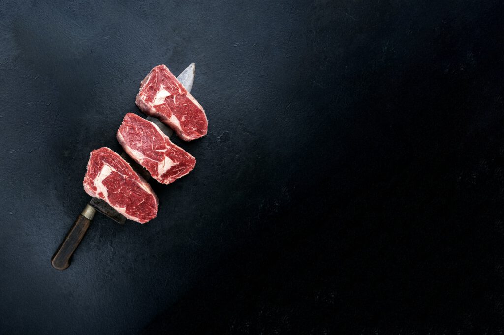 Three steaks on dark countertop